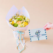 Pack Arreglo de flores amarillas Colvin, con envoltorio a cuadros menta y vainilla, con una mano sosteniendo una tarjeta floral. 
