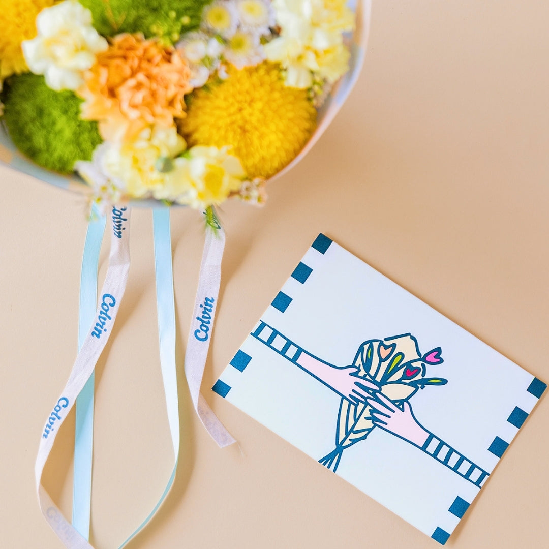 Detalle del pack Arreglo de flores amarillas Colvin, con envoltorio a cuadros menta y vainilla, con una tarjeta floral.