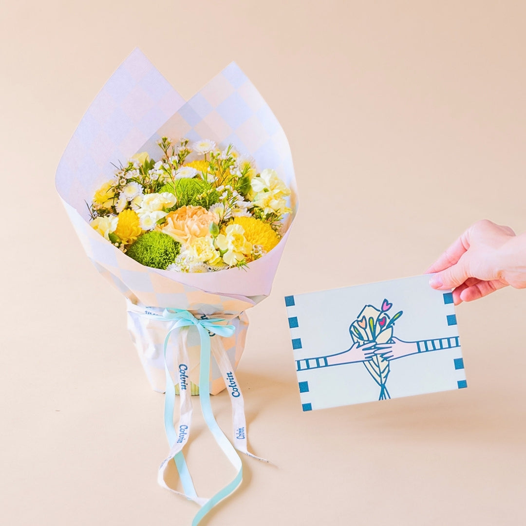 Pack Arreglo de flores amarillas Colvin, con envoltorio a cuadros menta y vainilla, con una mano sosteniendo una tarjeta floral. 