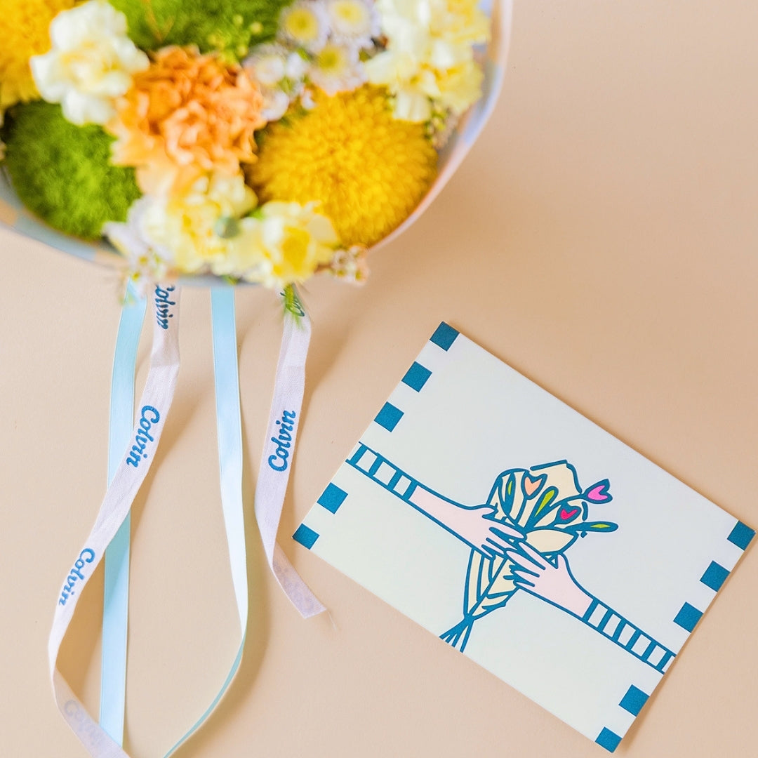 Detalle del pack Arreglo de flores amarillas Colvin, con envoltorio a cuadros menta y vainilla, con una tarjeta floral. 