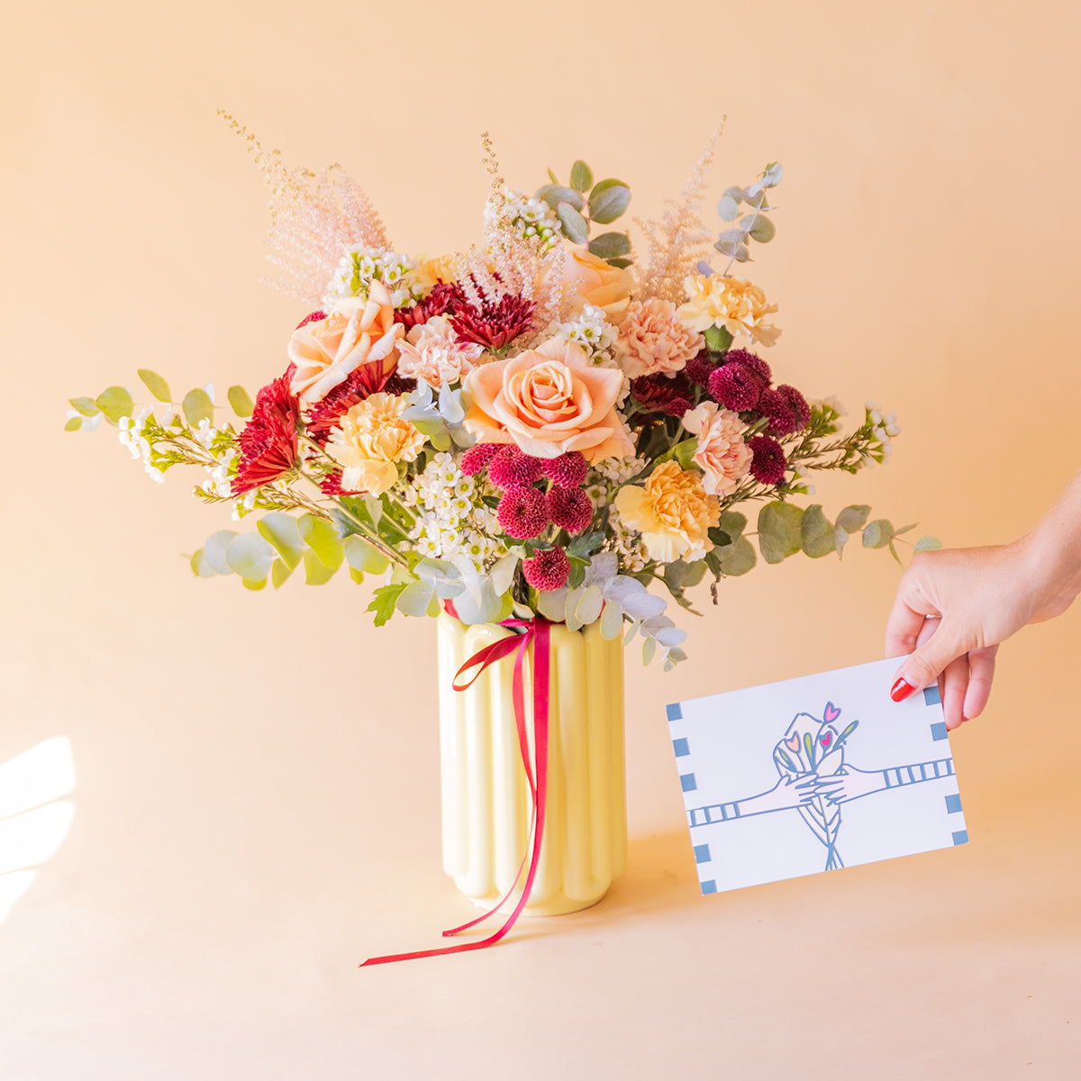 mano sosteniendo la tarjeta Más que Flores junto al ramo en jarrón