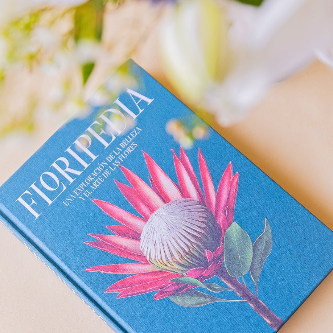 	Portada del libro Floripedia de Colvin con ilustración de protea rosa sobre fondo azul, junto a ramo de flores blancas desenfocado
