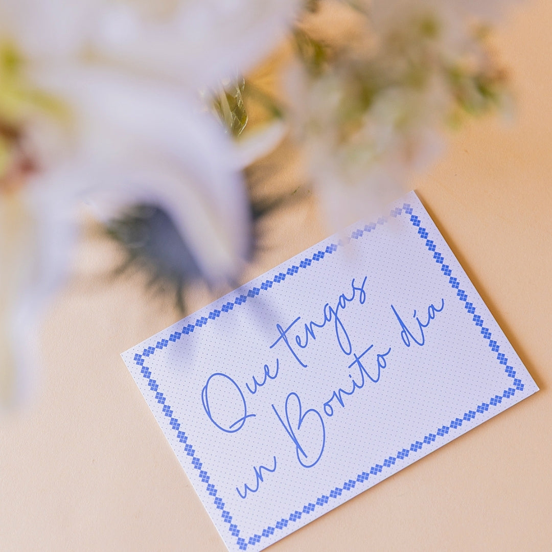 Detalle de tarjeta Más que Flores con mensaje manuscrito "Que tengas un Bonito día" junto a ramo de flores blancas Colvin