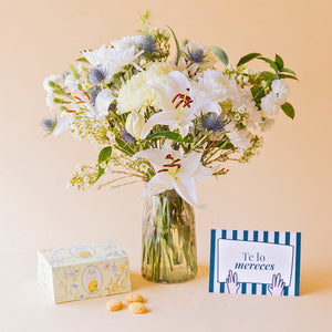 Ramo de flores blancas de Colvin en jarrón de cristal con lirios, crisantemos, eryngium azul y wax flower, junto a caja de galletas Loison de limón y tarjeta "Te lo mereces"