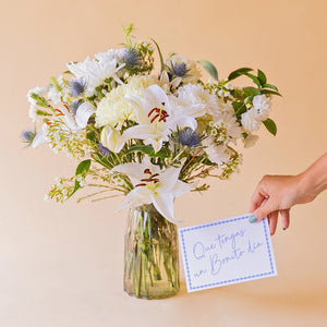 Ramo de flores blancas Colvin con lirio, crisantemo y eryngium en jarrón Gala, con mano sosteniendo tarjeta "Que tengas un Bonito día"