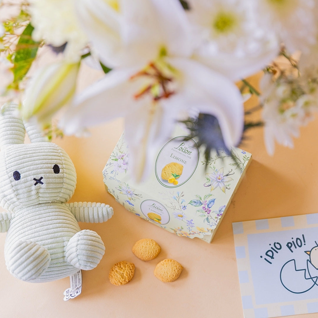 Peluche Miffy de corduroy blanco junto a caja de galletas Loison de limón y tarjeta "¡Pío Pío!" con ramo de flores blancas de Colvin