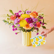 Ramo de flores coloridas Colvin con rosas salmón, crisantemos amarillos y claveles fucsia en jarrón Alba amarillo, con tarjeta de limones