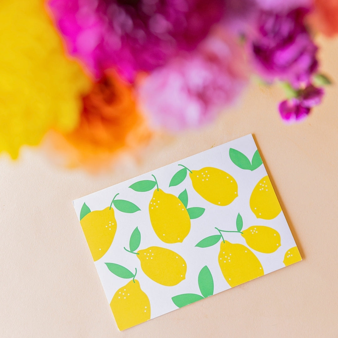 Detalle de tarjeta Más que Flores con estampado de limones amarillos y verdes, junto a ramo de flores coloridas Colvin
