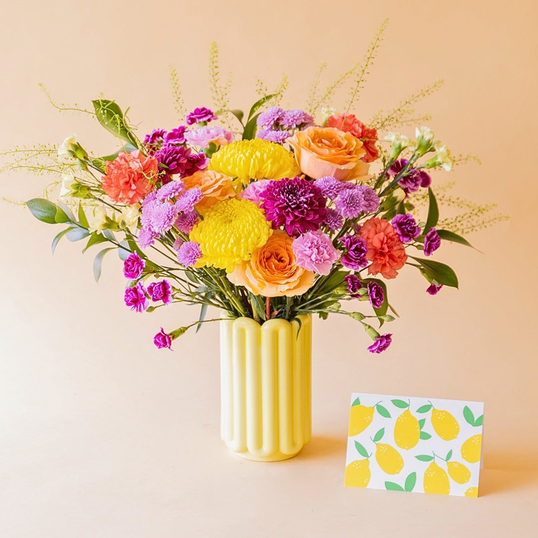 Ramo de flores coloridas Colvin con rosas salmón, crisantemos amarillos y claveles fucsia en jarrón Alba amarillo, con tarjeta de limones