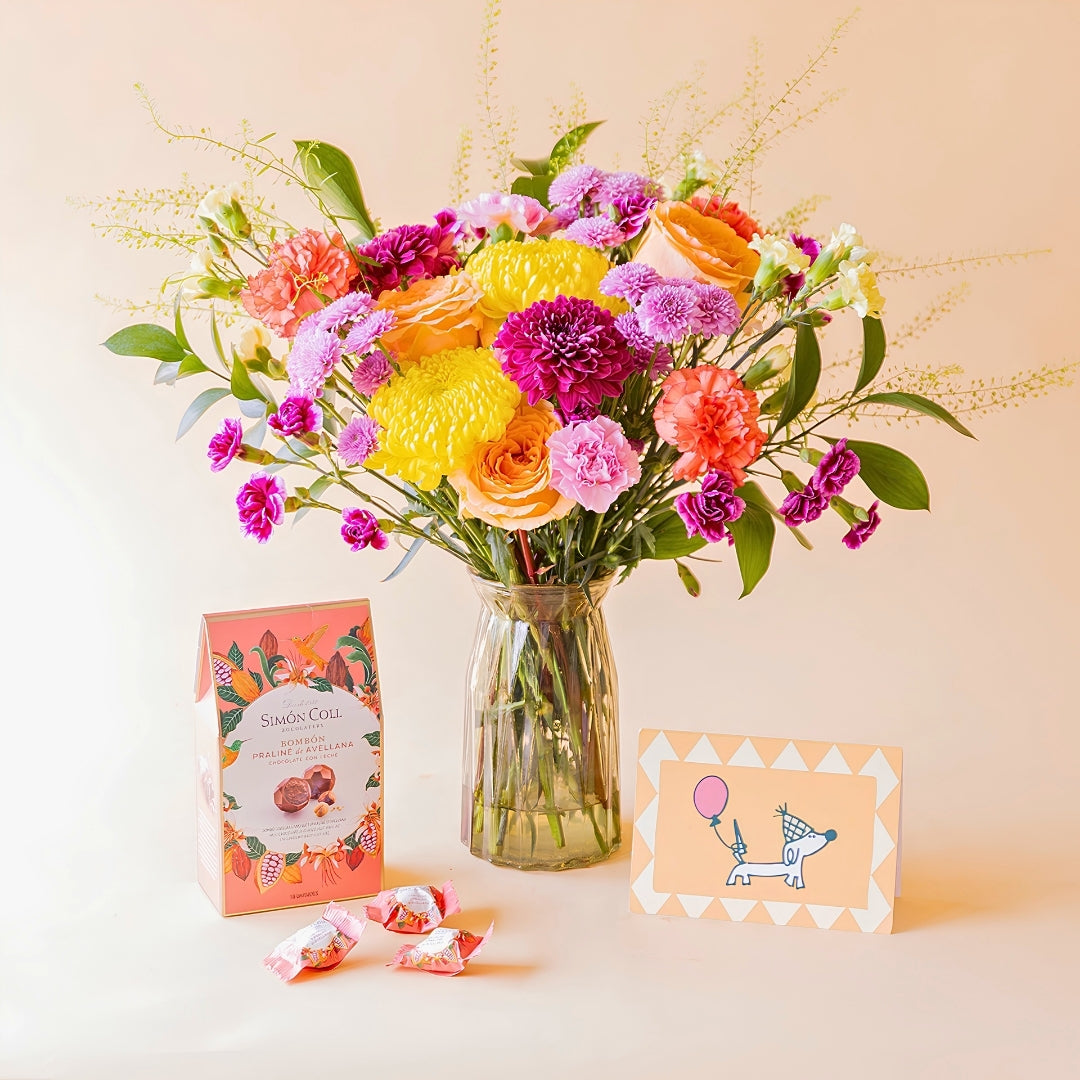 Ramo de flores coloridas de Colvin en jarrón de cristal con bombones Simón Coll pralinés de avellana y tarjeta de cumpleaños con perrito