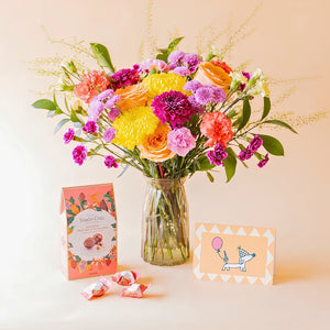Ramo de flores coloridas de Colvin en jarrón de cristal con bombones Simón Coll pralinés de avellana y tarjeta de cumpleaños con perrito