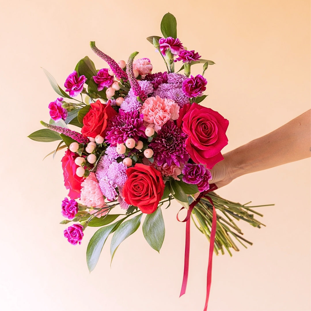 Mano sosteniendo ramo de flores rojas de Colvin con rosas rojas, crisantemos lilas, claveles fucsia y bayas blancas