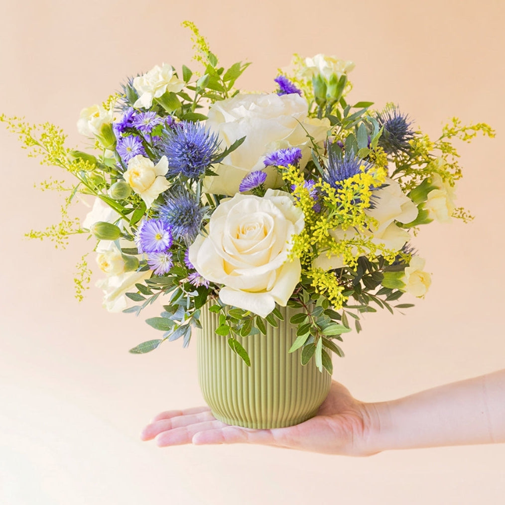 El Mágico - Arreglo floral con rosas crema con base verde oliva presentado sobre una mano