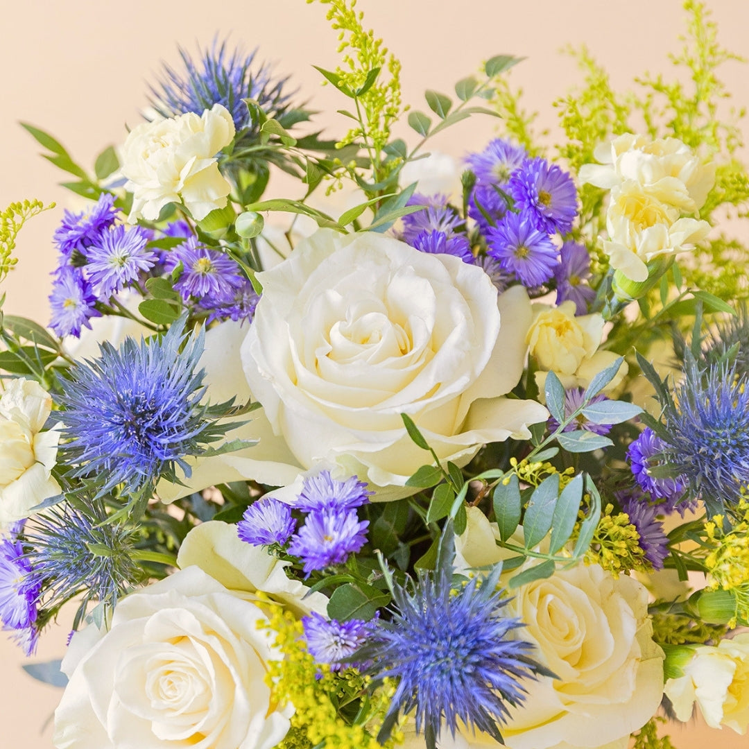 Detalle del arreglo Mágico Colvin con rosa blanca en arreglo floral con aster morado y eryngium azul