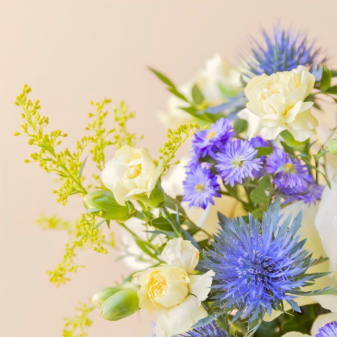 Detalle del arreglo Mágico Colvin con rosa blanca en arreglo floral con aster morado y eryngium azul