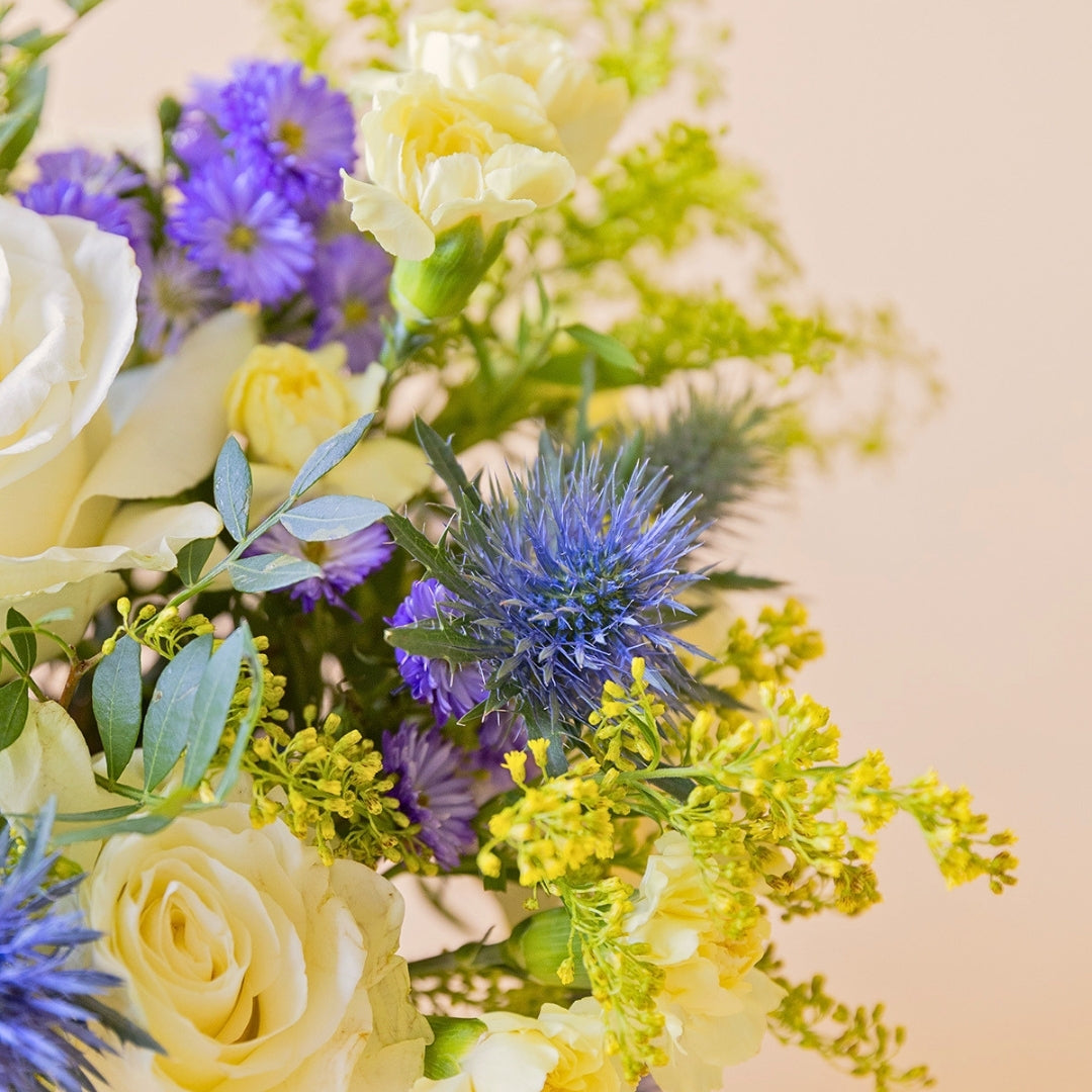 Detalle del arreglo Mágico Colvin con rosa blanca en arreglo floral con aster morado y eryngium azul
