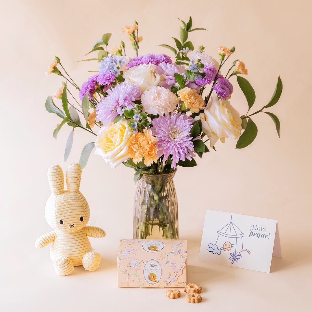 Ramo de flores pastel de nacimiento de Colvin en jarrón de cristal con crisantemos lilas, rosas amarillas, claveles melocotón y no me olvides, junto a peluche Miffy amarillo, galletas Loison Estrello Caramel y tarjeta "¡Hola peque!"