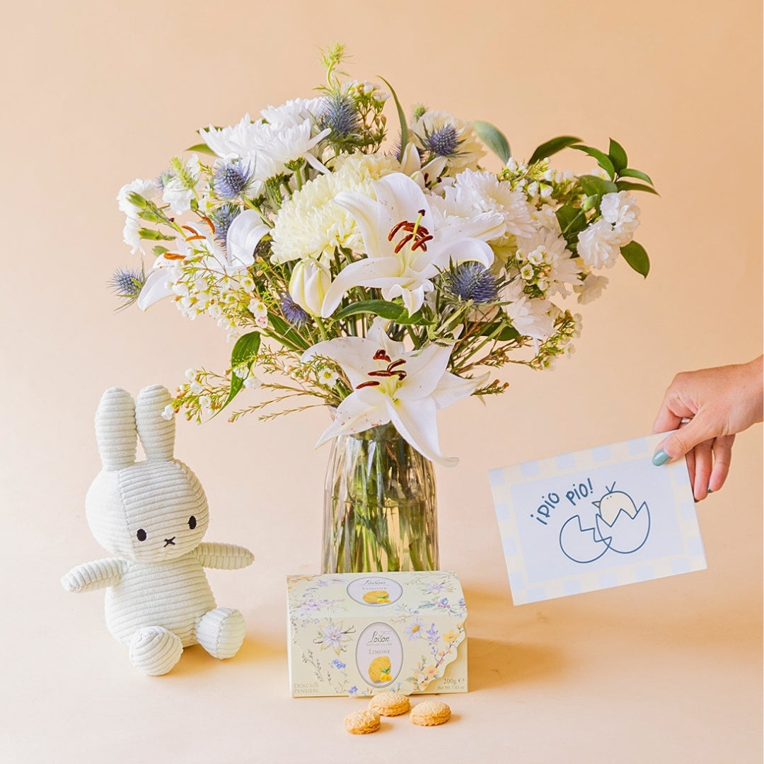 Ramo de flores blancas de Colvin en jarrón de cristal con lirios, crisantemos, eryngium azul y wax flower, junto a peluche Miffy, galletas y tarjeta "¡Pío Pío!"