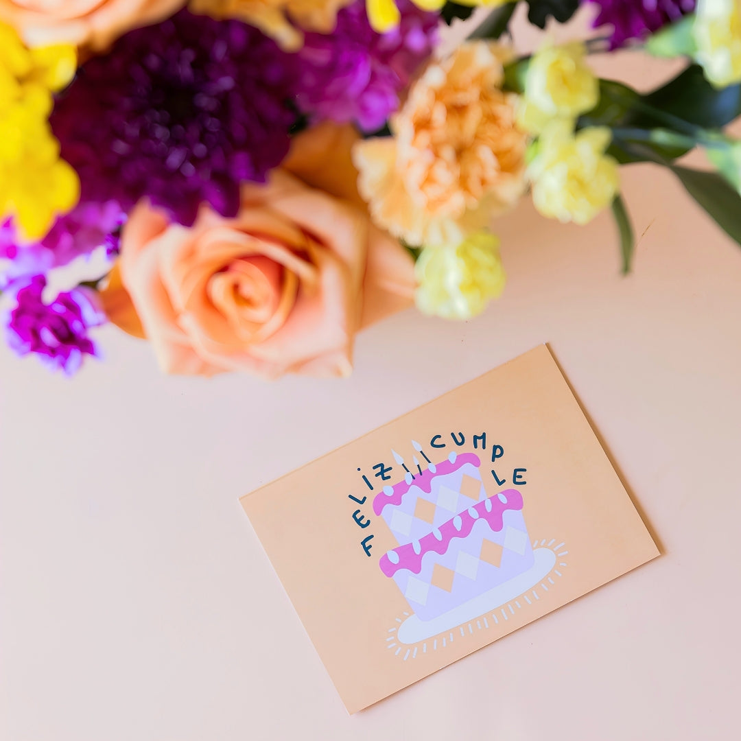 Detalle del ramo de flores frescas El Colorido de Colvin, una tarjeta de felicitación de cumpleaños con la frase "Feliz Cumple" y una tarta ilustrada, sobre fondo beige.
