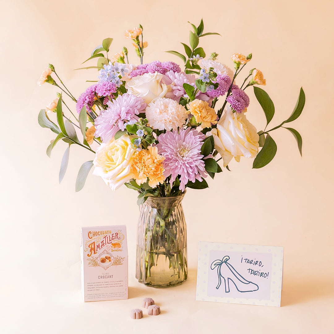 Ramo de flores pastel de Colvin en jarrón de cristal con crisantemos lilas, rosas blancas, claveles melocotón y no me olvides, junto a bombones Amatller Crocant y tarjeta "¡Tariro, Tariro!"