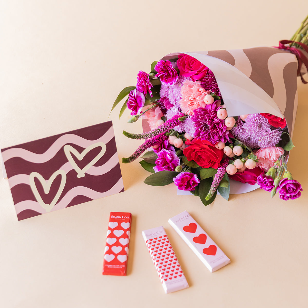 Ramo El Hechizo de Colvin en envoltorio de ondas burdeos junto a tarjeta de corazones y tres chocolatinas Simón Coll con packaging de corazones