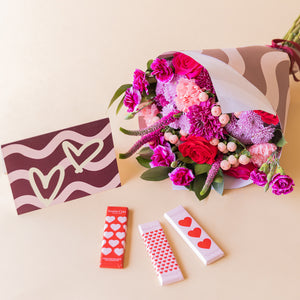 Ramo El Hechizo de Colvin en envoltorio de ondas burdeos junto a tarjeta de corazones y tres chocolatinas Simón Coll con packaging de corazones