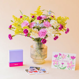 Ramo Bonito Recuerdo de Colvin con claveles fucsia, rosa, crema y solidago amarillo en jarrón acanalado dorado, junto a la Cheerz Box lila, fotos reveladas y tarjeta "Te Quiero", sobre fondo melocotón