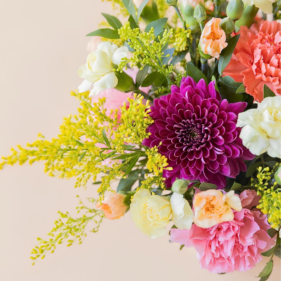 La Chispa - Detalle de arreglo floral con claveles amarillos y naranjas con crisantemos morados de Colvin.
