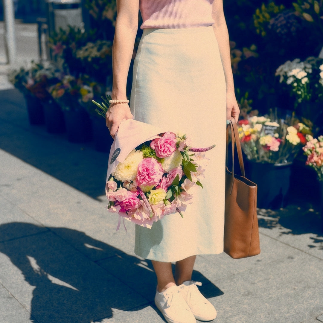 Mujer sosteniendo el ramo La Dolce Vita de Colvin con rosas rosas y flores silvestres, envuelto en papel rosa, frente a una floristería