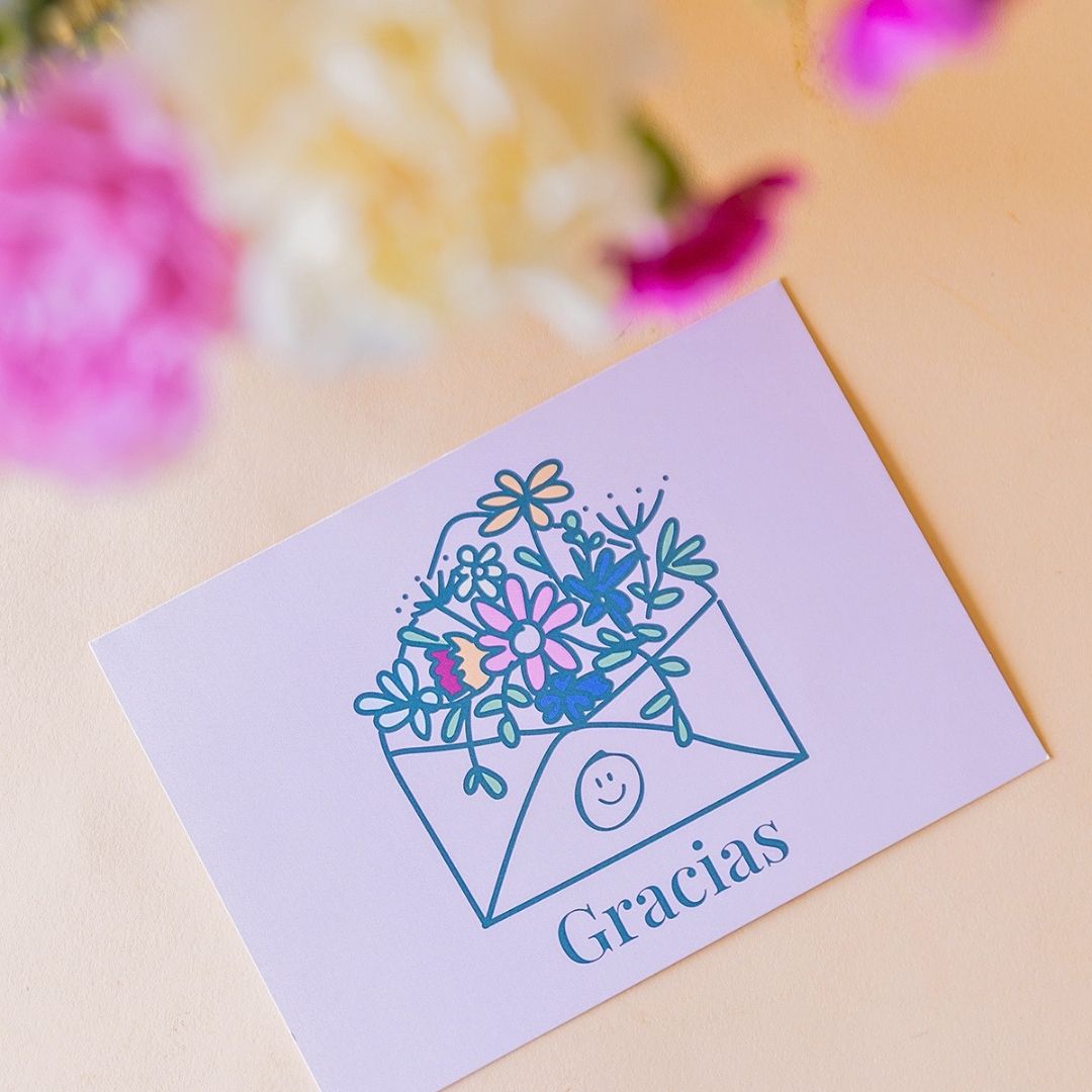 Detalle de la Tarjeta Gracias de Colvin con ilustración de sobre y flores, con claveles rosas y crema desenfocados al fondo