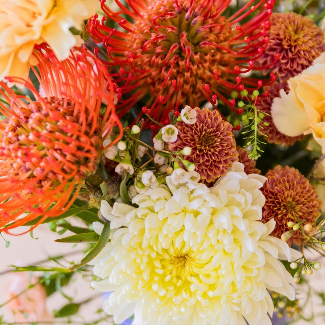 Detalle del ramo de verano de Colvin La Jarana con proteas alfiletero de color naranja, crisantemos y flores crema.