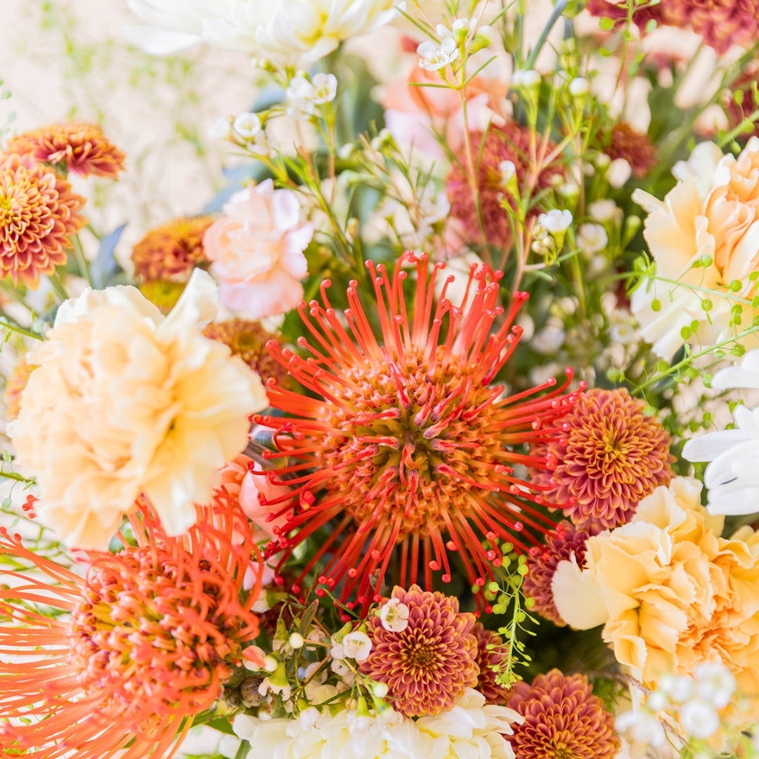 Detalle del ramo de verano de Colvin La Jarana con proteas alfiletero de color naranja, crisantemos y flores crema.