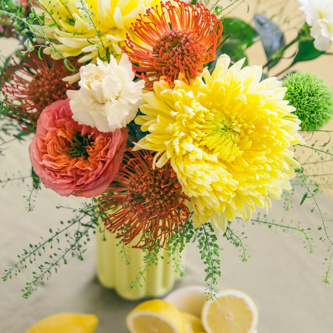 Ramo de flores frescas La Verbena de Colvin en un jarrón amarillo rodeado de limones.