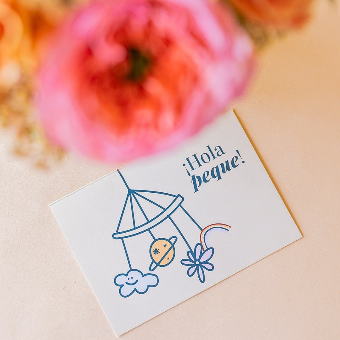 Detalle de tarjeta Más que Flores ¡Hola peque! con ilustración de móvil de cuna, junto a rosa garden rosa de Colvin