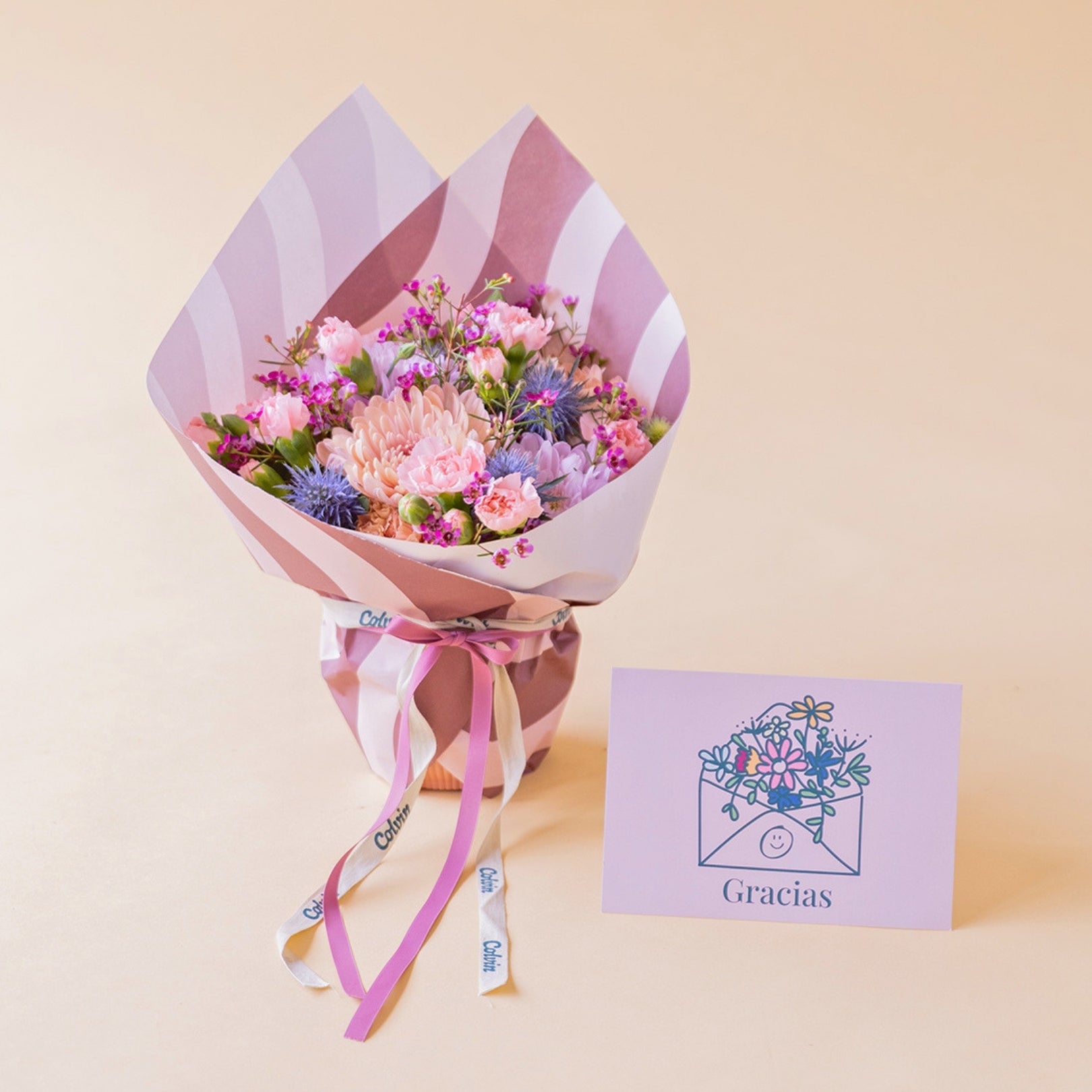 Pack de regalo Colvin con el arreglo floral Guiño en tonos azules y morados junto a una tarjeta dedicatoria de "Gracias".