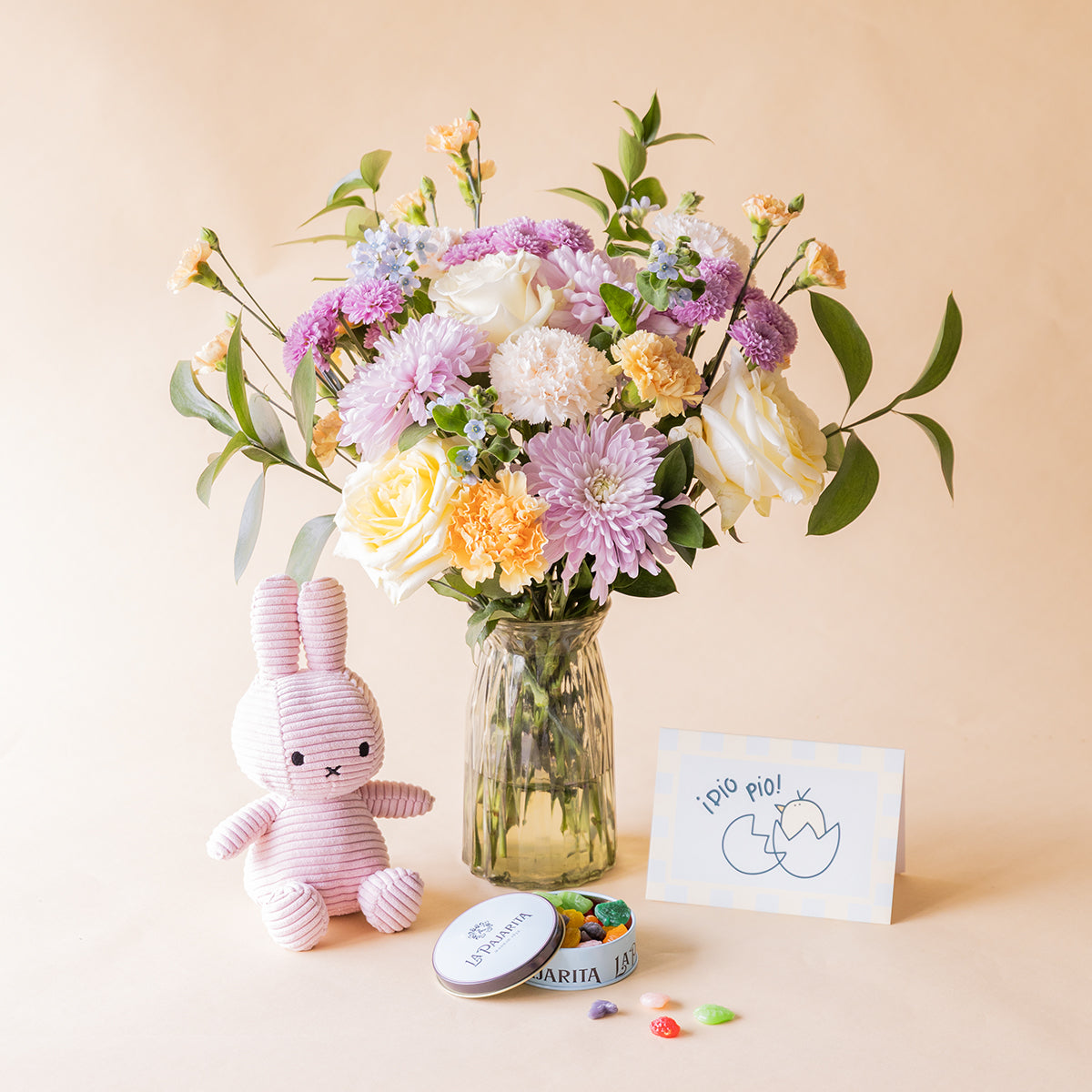 Ramo de flores pastel de nacimiento de Colvin en jarrón de cristal con crisantemos lilas, rosas amarillas, claveles melocotón y no me olvides, junto a peluche Miffy rosa, lata de gominolas La Pajarita y tarjeta "¡Pío Pío!"
