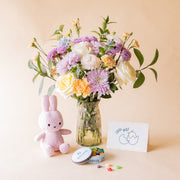 Ramo de flores pastel de nacimiento de Colvin en jarrón de cristal con crisantemos lilas, rosas amarillas, claveles melocotón y no me olvides, junto a peluche Miffy rosa, lata de gominolas La Pajarita y tarjeta "¡Pío Pío!"