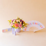 Arreglo de flores con abanico Fisura, velas arcoíris y protector solar Kream
