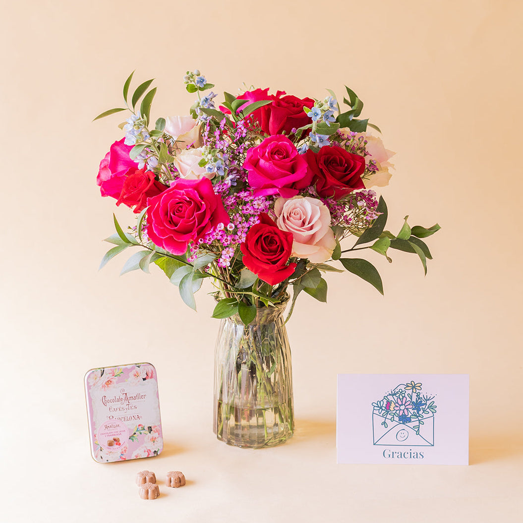 Ramo de rosas fucsias, rojas y rosa empolvado Colvin El Encanto en jarrón de cristal con lata de bombones Amatller y tarjeta Gracias sobre fondo beige