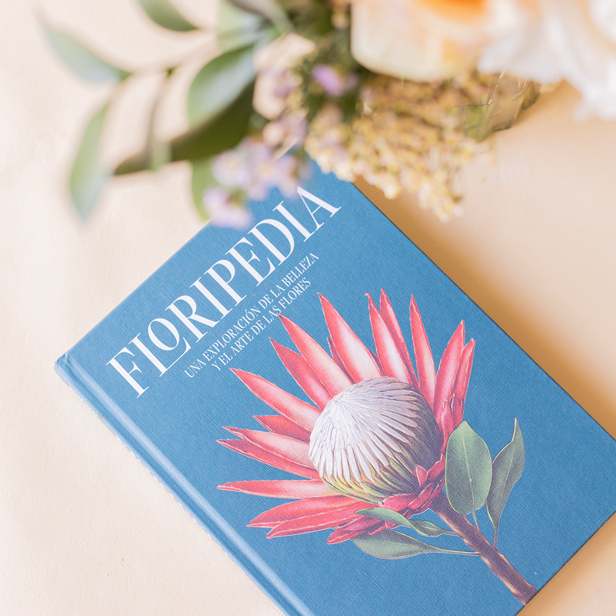 Portada del libro Floripedia de Colvin con ilustración de protea rosa sobre fondo azul, con ramo de flores desenfocado al fondo