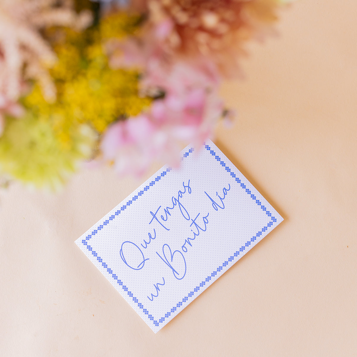 Detalle de la tarjeta Colvin Que tengas un Bonito día con borde azul y flores silvestres del ramo desenfocadas al fondo