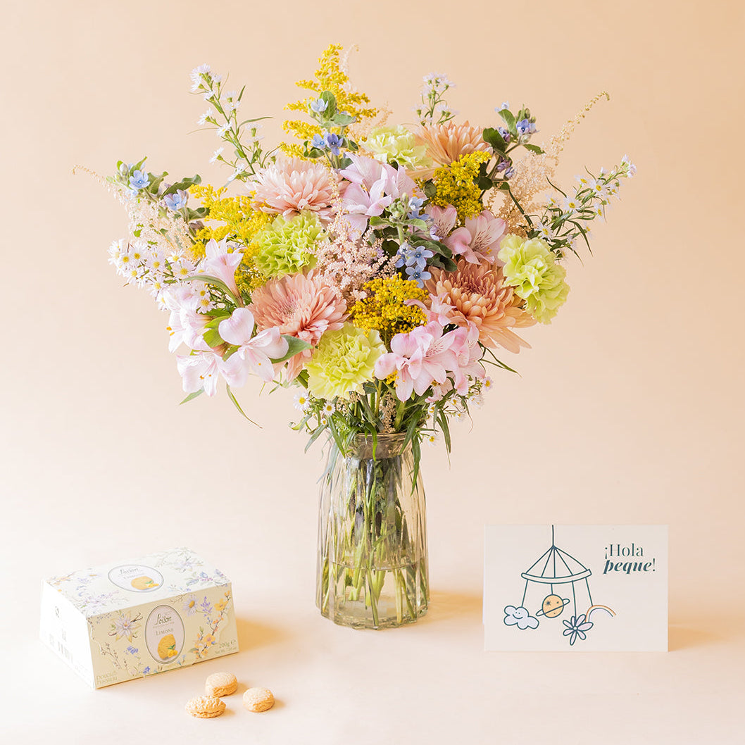 Ramo Colvin silvestre de crisantemos melocotón, alstroemerias rosas y flores silvestres en jarrón de cristal con caja de galletas Loison limón y tarjeta ¡Hola peque! sobre fondo beige