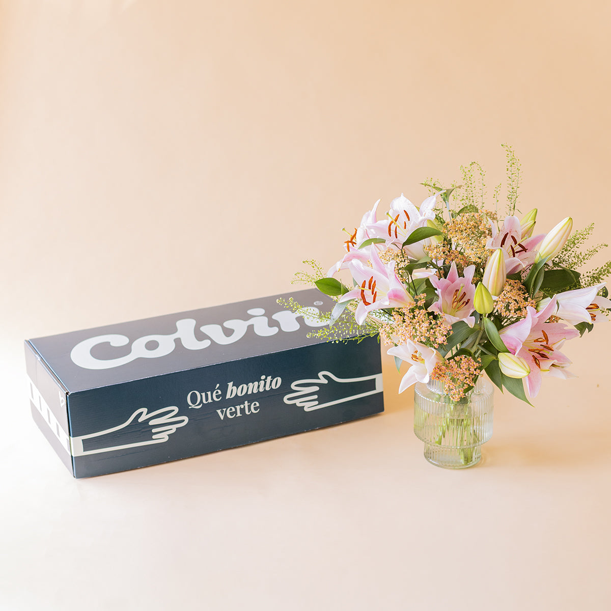 Caja de envío Colvin junto a ramo de lirios rosas en jarrón de cristal
