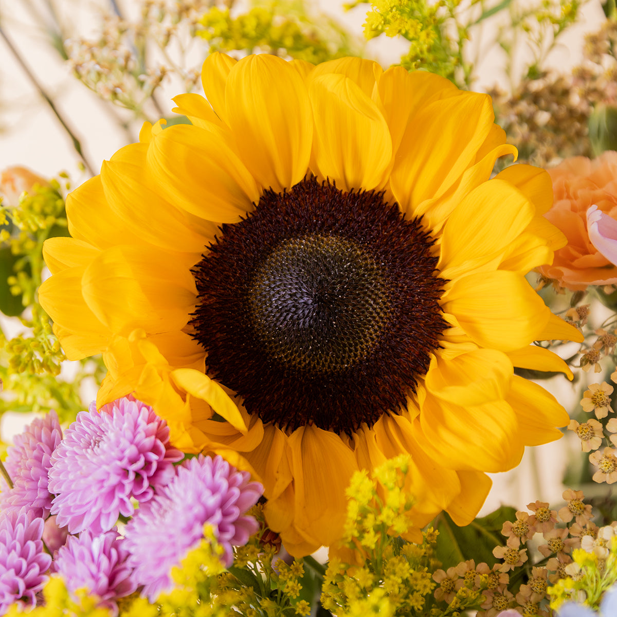 Primer plano de girasol amarillo del ramo Colvin con crisantemos lilas, solidago y flores silvestres de fondo