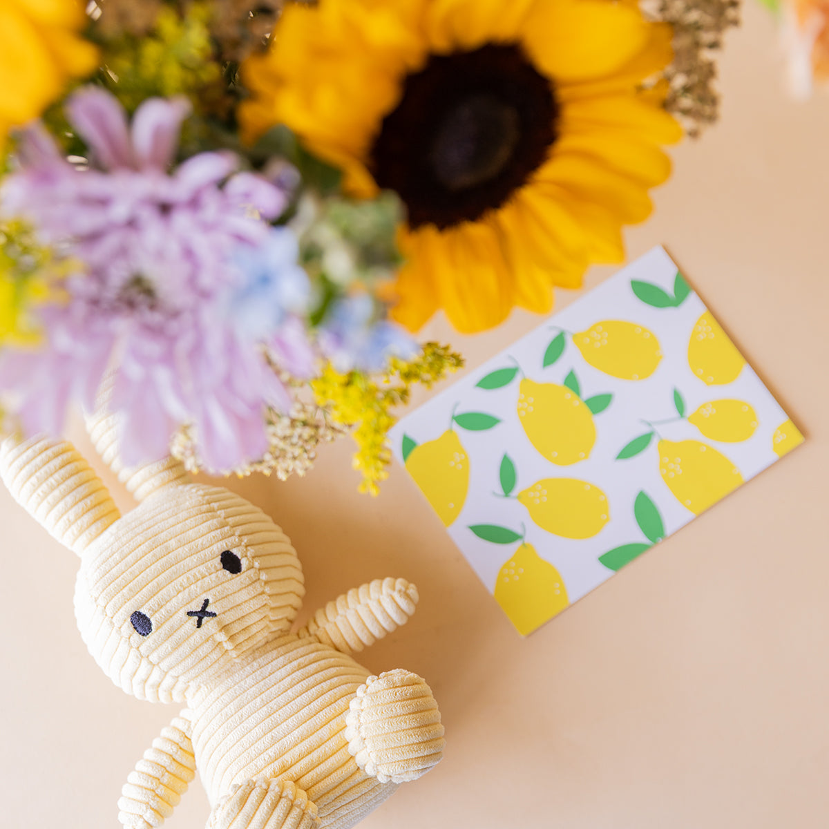 Detalle del ramo de girasoles Colvin con peluche Miffy de corduroy crema y tarjeta ilustrada con limones