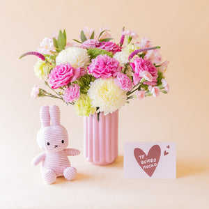Ramo de rosas fucsias, crisantemos blancos, alstroemeria rosa y veronica lila de Colvin en jarrón acanalado rosa con peluche Miffy lila y tarjeta Te quiero mucho, sobre fondo melocotón