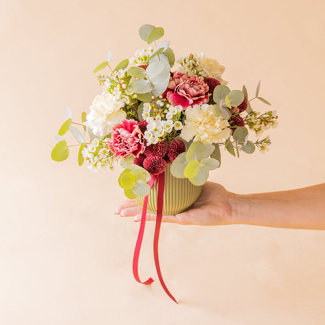 	Mano sosteniendo el arreglo La Bellota con claveles rosas, blancos y flor de cera — Colvin
