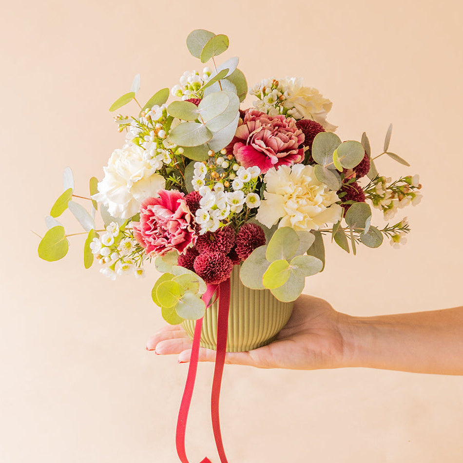 	Mano sosteniendo el arreglo La Bellota con claveles rosas, blancos y flor de cera — Colvin