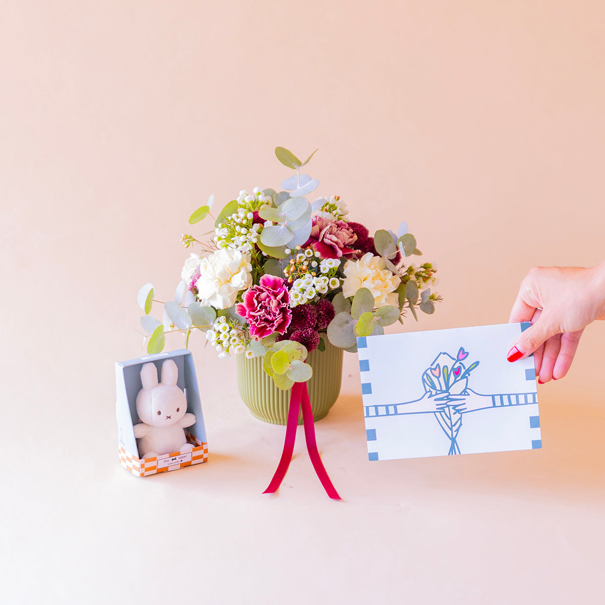 Mano con tarjeta ilustrada junto a arreglo de claveles con mini peluche — Colvin
