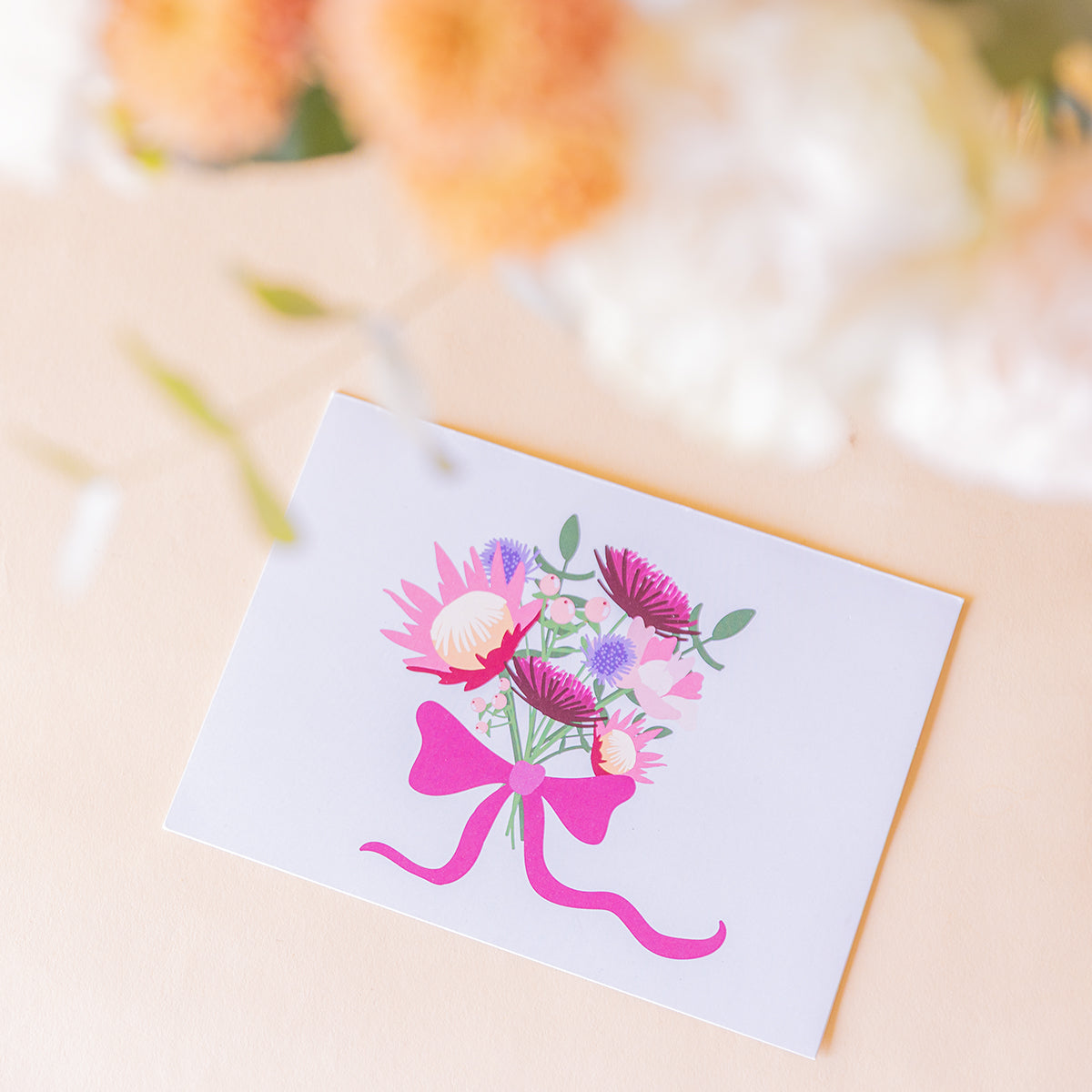 detalle macro de la tarjeta Proteas con ilustración de ramo y lazo fucsia, ramo desenfocado al fondo
